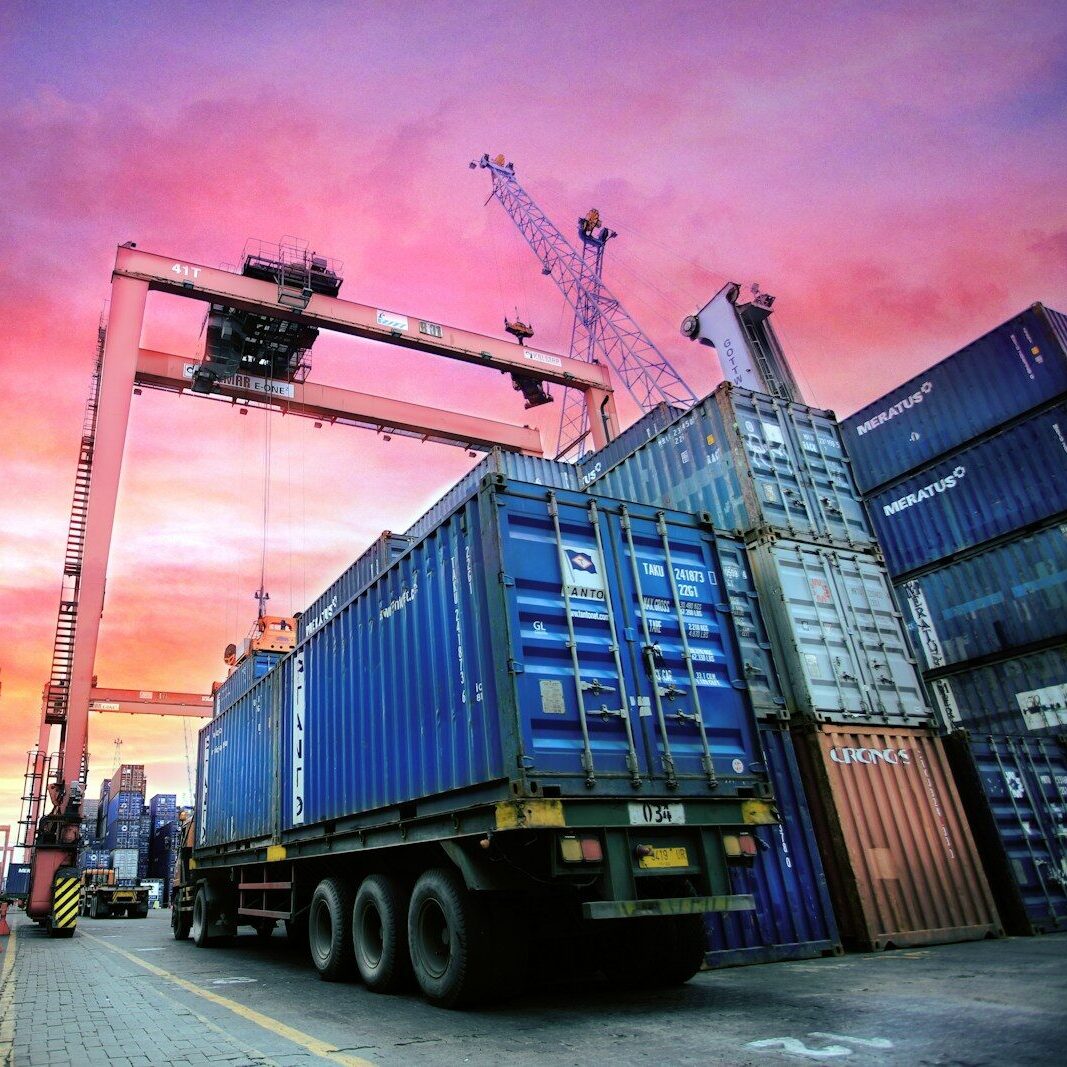 Container di spedizione impilati in un porto trafficato al tramonto.